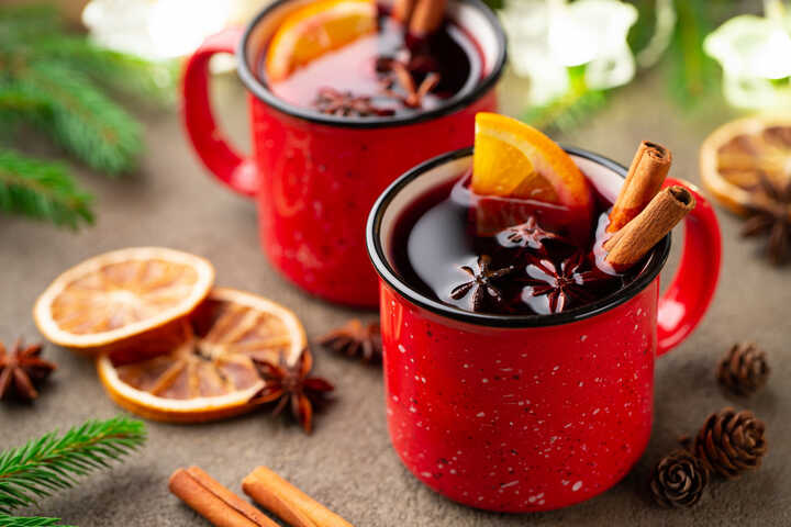 Non-alcoholic mulled wine in red mugs garnished with cinnamon sticks, star anise and orange slices