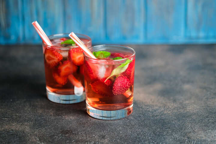 Two glasses of red drink, with sliced strawberries and basil leaves