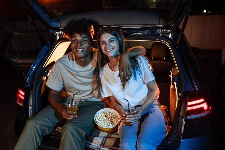 A young couple sat in the boot of their car with popcorn, watching a drive thru movie.