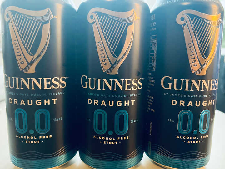 Guinness Draught 0.0% Alcohol Free Stout - 3 cans in a row, with the light reflecting off of them